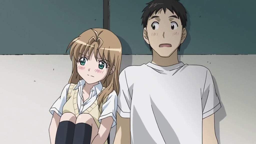 Yamada e Kosuda sentados no chão e encostados em uma parede, ambos estão tímidos e envergonhados.